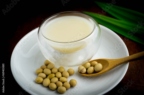 soy milk in transparent round glass decorating with dried soy beans and pandan leaves in black background