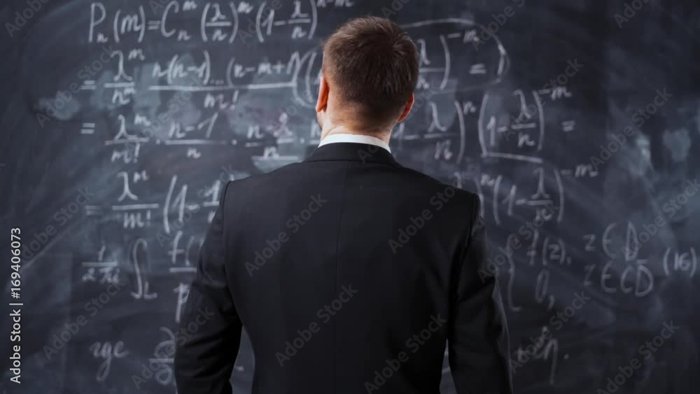 Back middle shot of male against chalk board with mathematics formula equations. He thinking about solutions and try to understand high university task. Back middle shot of male against chalk board with mathematics formula equations. He thinking about solutions and try to understand high university task.