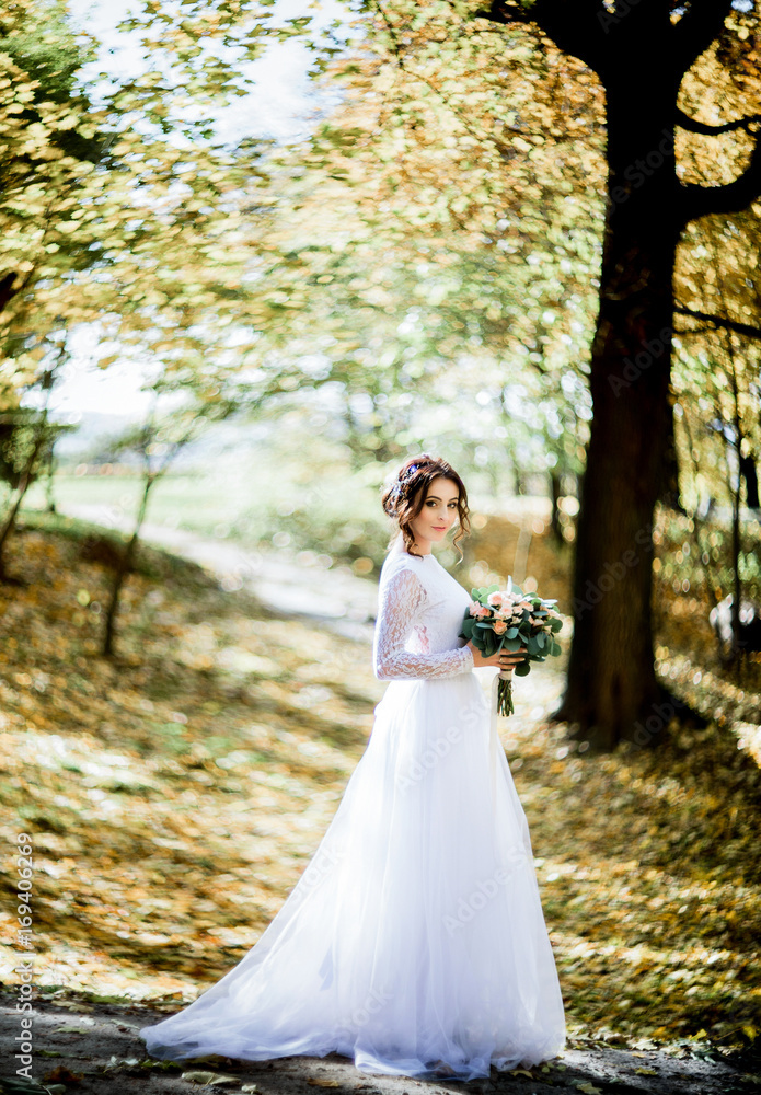 Beautiful bride with black curls poses on path in autumn forest Beautiful bride with black curls poses on path in autumn forest