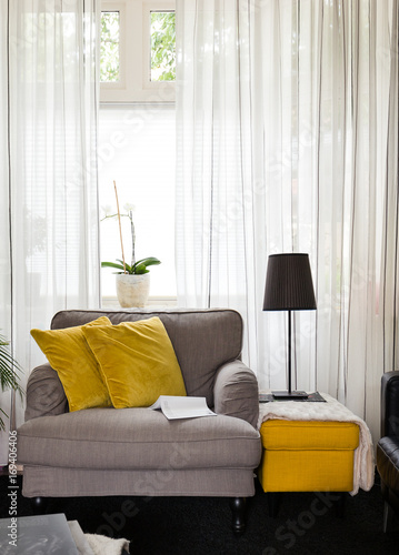 Cosy fabric armchair or love seat with yellow pillows in bright lightened living room photo