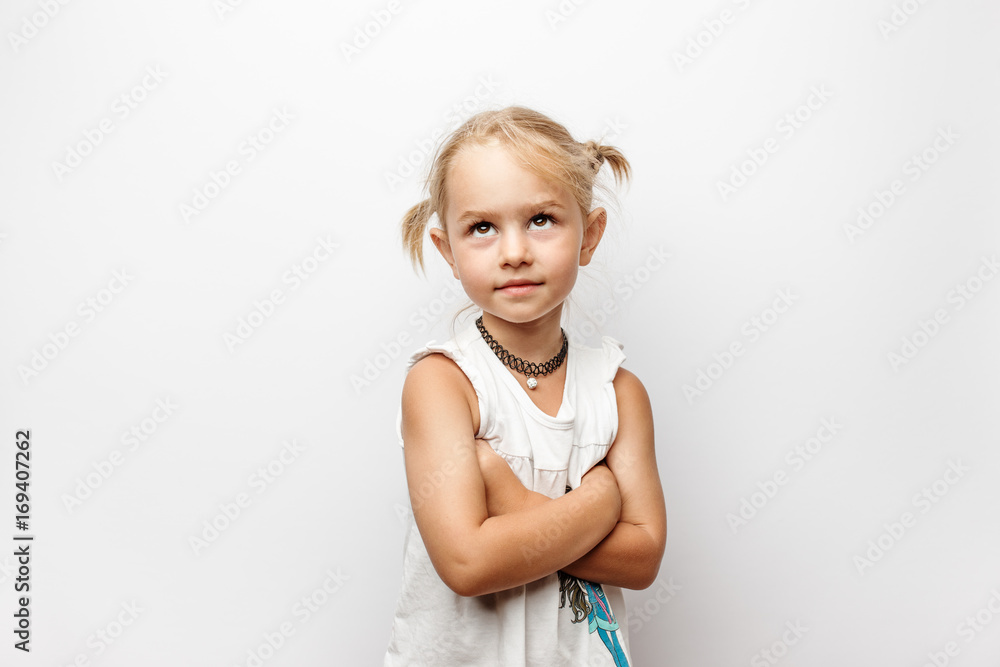 Little girl in white dress with crossed arms looks up on white background Little girl in white dress with crossed arms looks up on white background