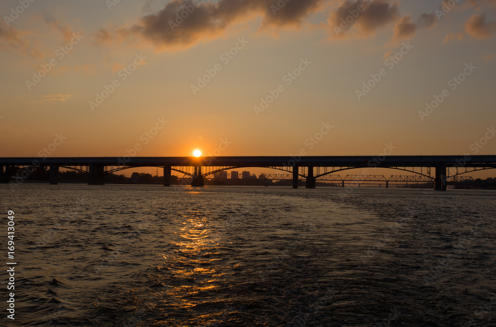 The silhouette of the bridge against the setting sun and the river