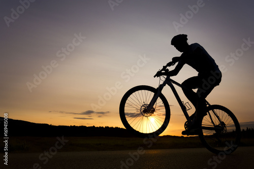 Silhouette of boy on the bike. Young cyclist is jumping on his bike during susnet. Fore wheel is over the horizon.