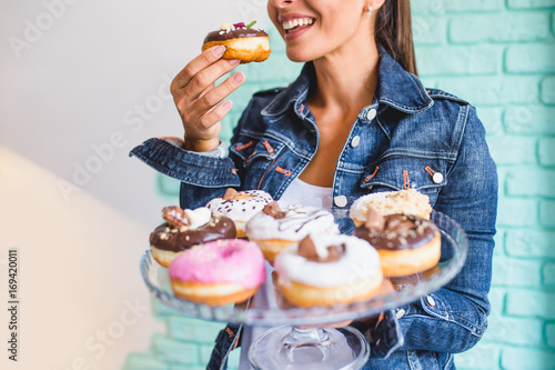 Beautiful young woman enjoying in delicious glazed and decorated donuts. Selective focus on hand holding donut.