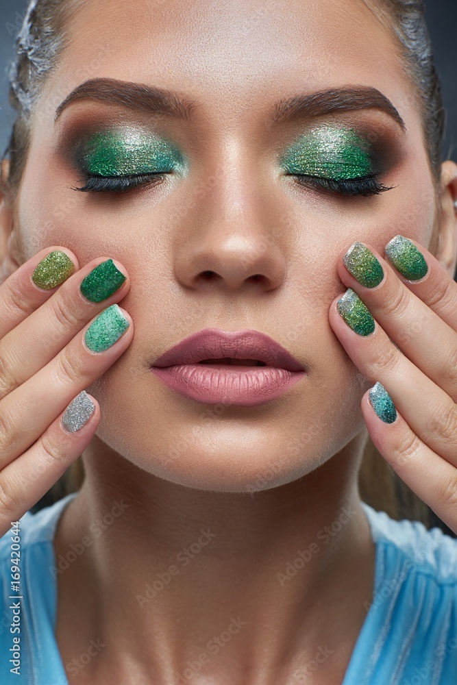 Fototapeta premium Front view of attractive brunette woman with perfect bronze skin, shiny manicure, makeup in green colors. Beautiful girl with plump lips, carried skin, touching showing nails. Beauty concept.
