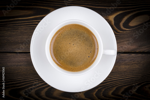 Overhead view of a freshly brewed mug of espresso coffee on rustic wooden background with woodgrain texture. Coffee break style