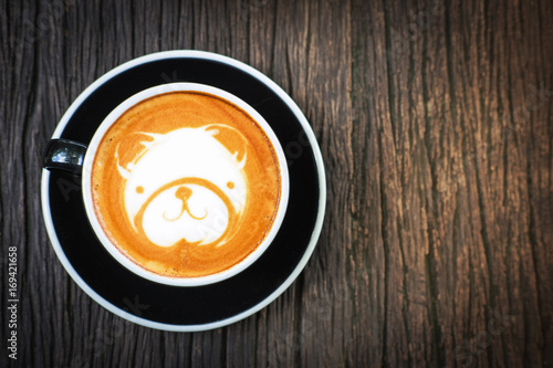 Bear face latte art coffee in black cup on old wooden desk , top view and copy space