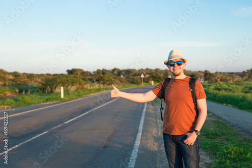 Man with Backpacks in casual Travel Clothes walking along road ,Road hitch-hiking. Traveler standing at the highway hitching © satura_