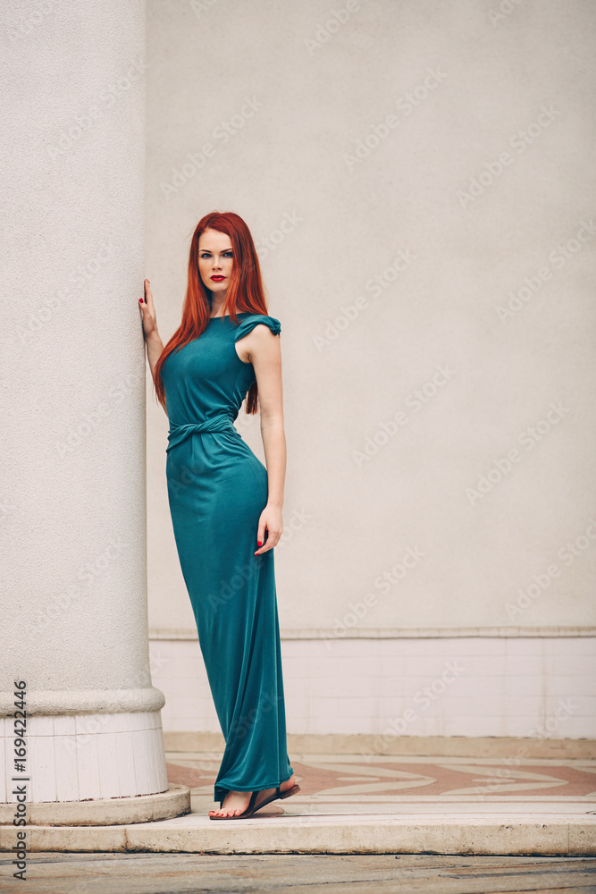 Portrait of a beautiful red-haired young woman in a green dress next to a column Portrait of a beautiful red-haired young woman in a green dress next to a column
