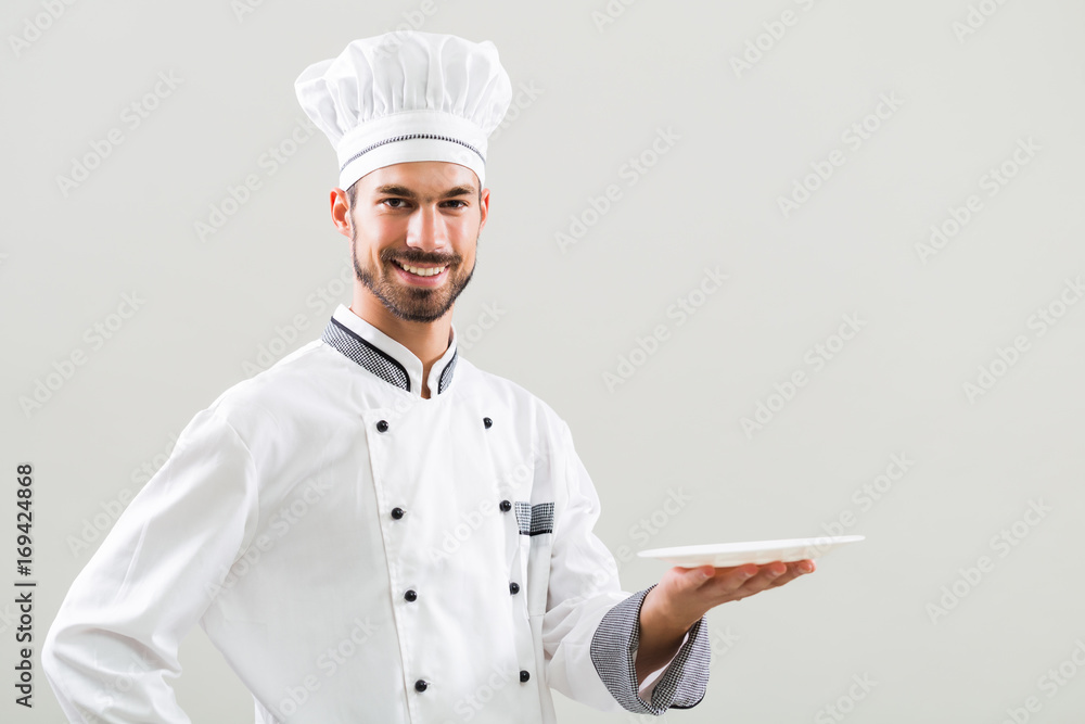 Smiling chef is holding plate on gray background. Smiling chef is holding plate on gray background.