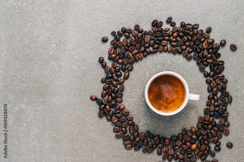 Naklejka premium Black coffee with cream on a gray background surrounded by coffee beans, top view.