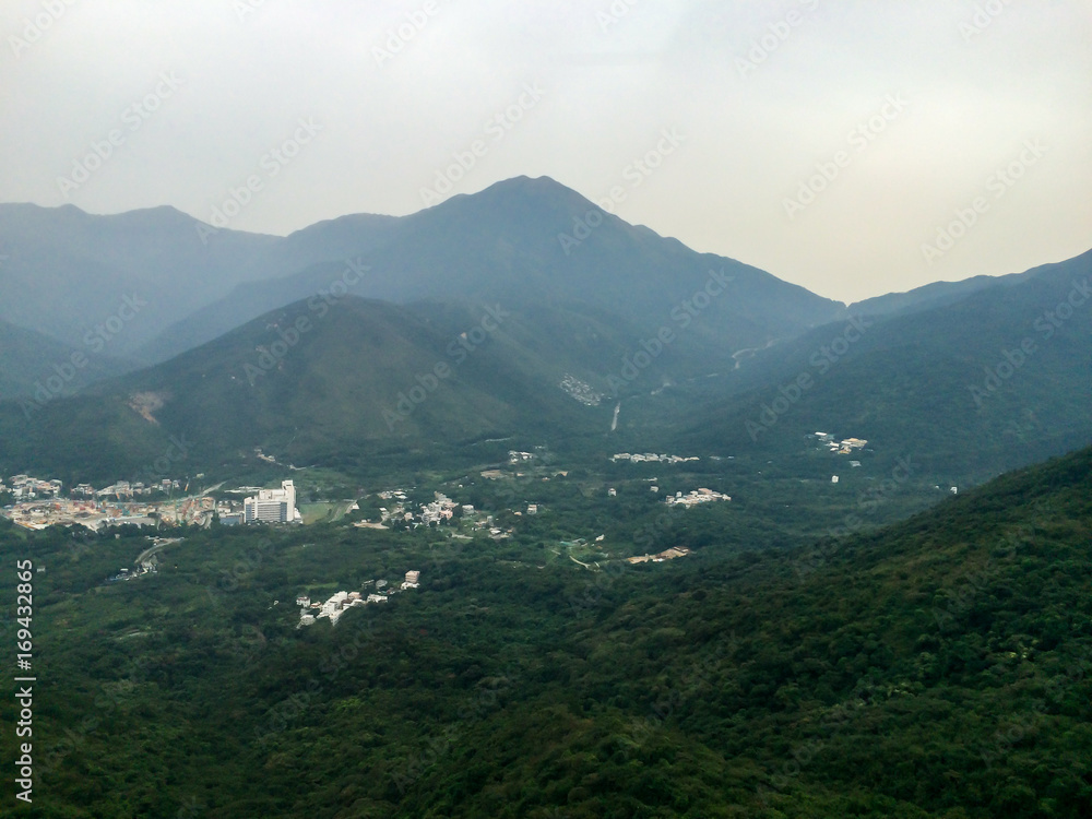 Foggy mountains covered in green forest trees with foggy sky as background and small city building between mountains