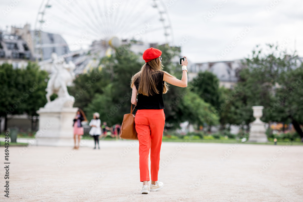 Young woman in red cap and pants walking in Tuileries park with ferry wheel on the background in Paris Young woman in red cap and pants walking in Tuileries park with ferry wheel on the background in Paris