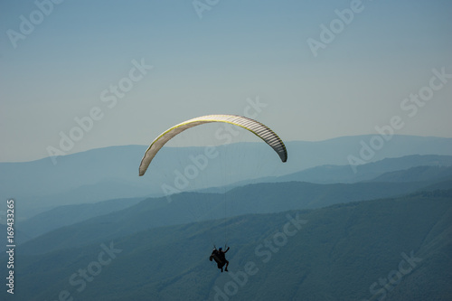 A paragliding tandem flies over a mountain valley on a sunny summer day. Paragliding in the Carpathians in the summer.