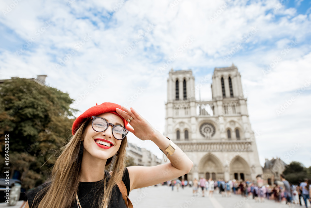 Portrait of a young woman tourist in red cap standing in front of the famous Notre Dame cathedral in Paris