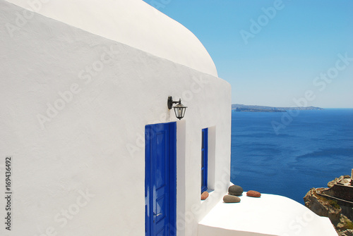 A small bell tower on the background of the dark blue sea in Santorini island. At the bottom of the water can be seen a small fishing boat