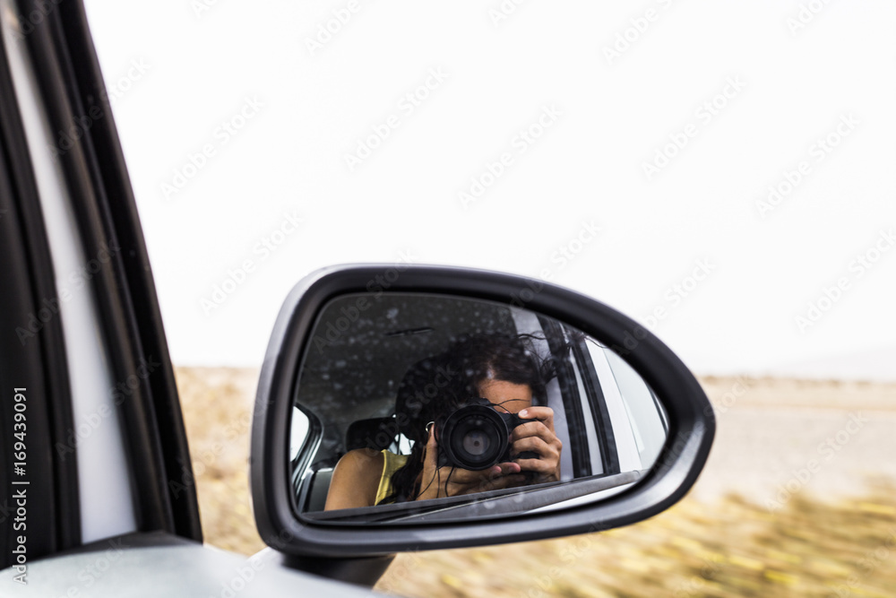 young woman taking a photo from a rear view mirror of a car. Summer. Lifestyle