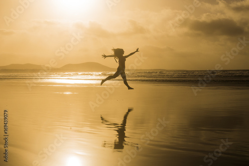 silhouette of a young beautiful woman jumping at the beach by the shore. Sunset. Yellow sky. Lanzarote, Canary islands