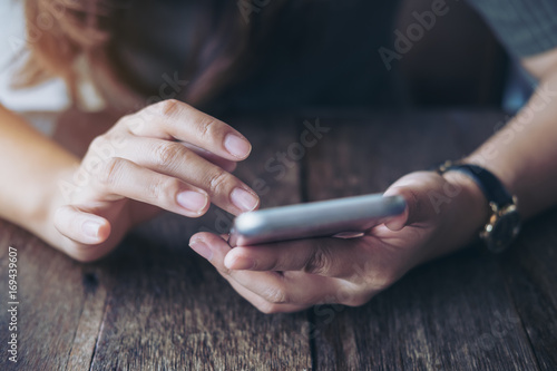 Closeup image of a woman s hands holding   using and pointing at smart phone on wooden table in vintage cafe