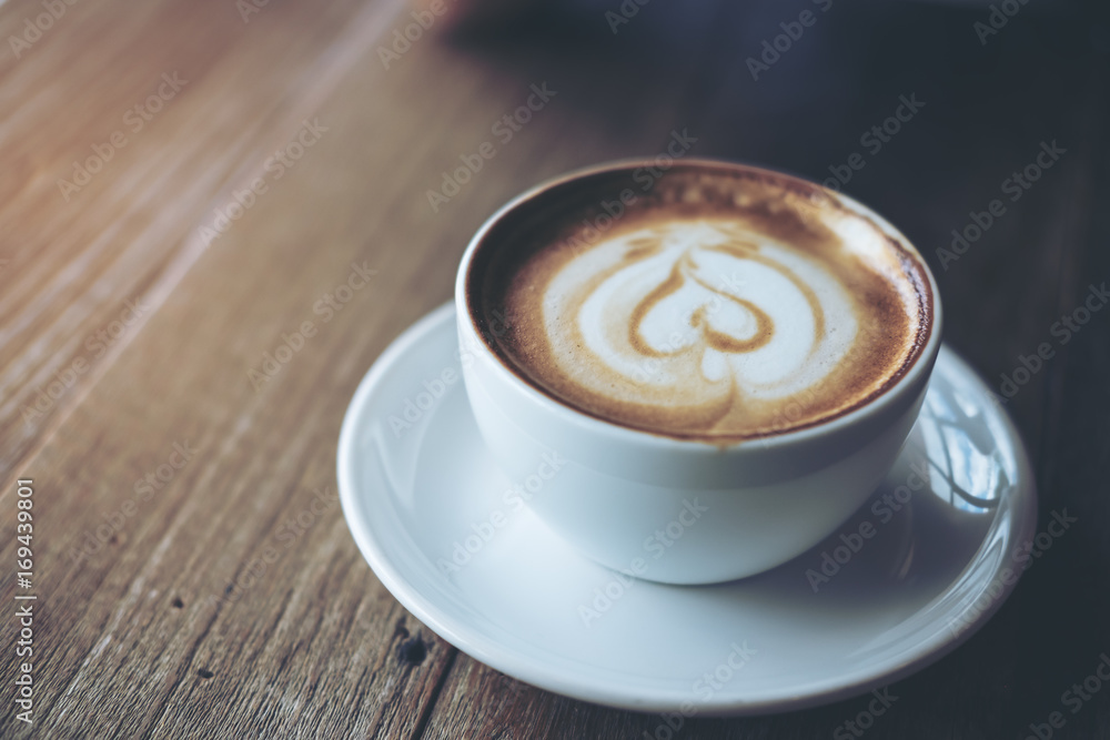 Closeup image of a white cup of hot latte coffee on vintage wooden table in cafe Closeup image of a white cup of hot latte coffee on vintage wooden table in cafe