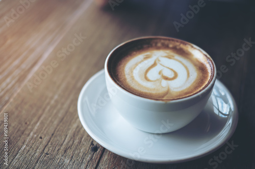 Closeup image of a white cup of hot latte coffee on vintage wooden table in cafe