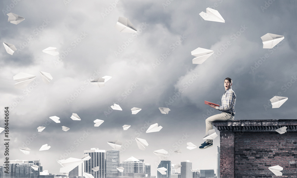 Handsome student guy on roof edge reading book and paper planes Handsome student guy on roof edge reading book and paper planes