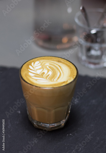 Flat white coffee on a shale plate in a transparent rox glass photo