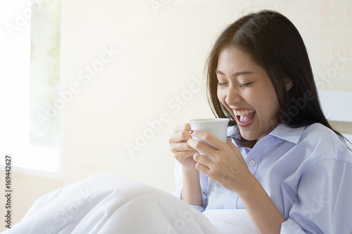 Happy Asian woman drinking coffee on bed