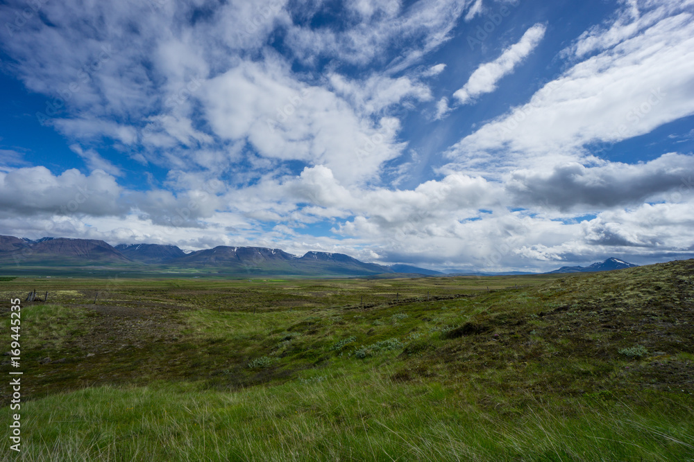 Iceland - Fantastic open range with snow covered mountains behind green flat landscape and blue sky