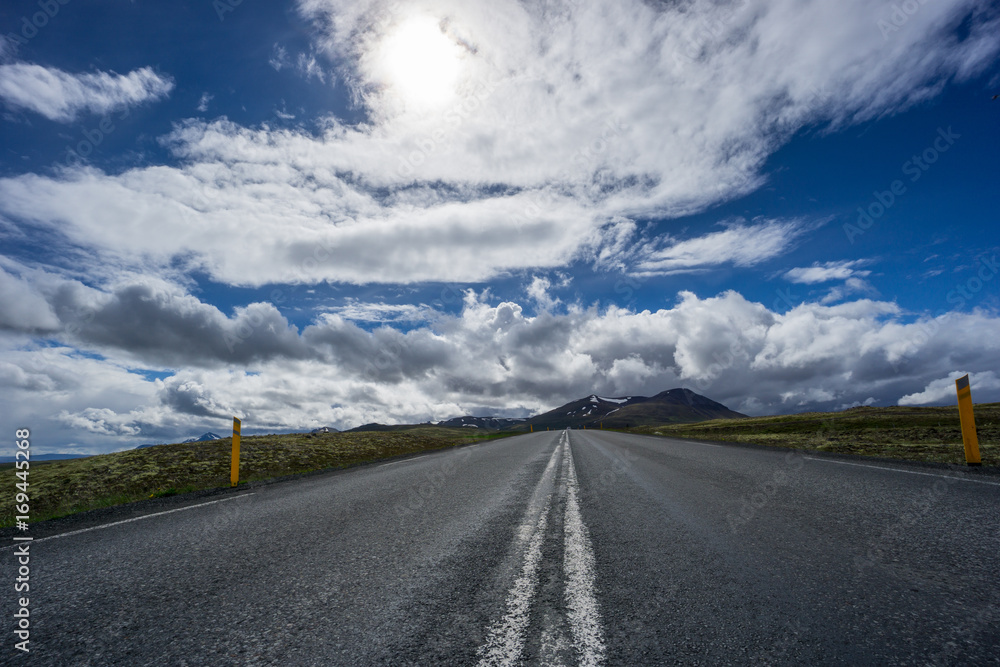 Iceland - Sunshine over straight road between icelandic volcanic mountainous green landscape Iceland - Sunshine over straight road between icelandic volcanic mountainous green landscape
