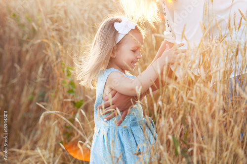 Little girl on a gold wheat field walking in the sunset. Happy four years old girl smiling and laughing in summer day at nature