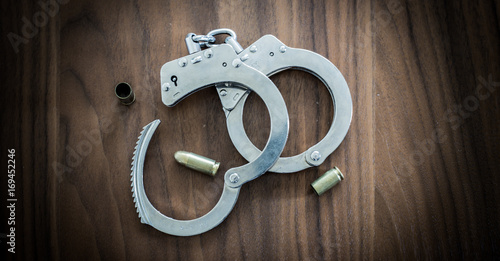 Golden bullet shells and police handcuffs for catching criminals half opened and fighting crime laying on the wooden ground. Prevention of crime and catching criminals handcuffed.