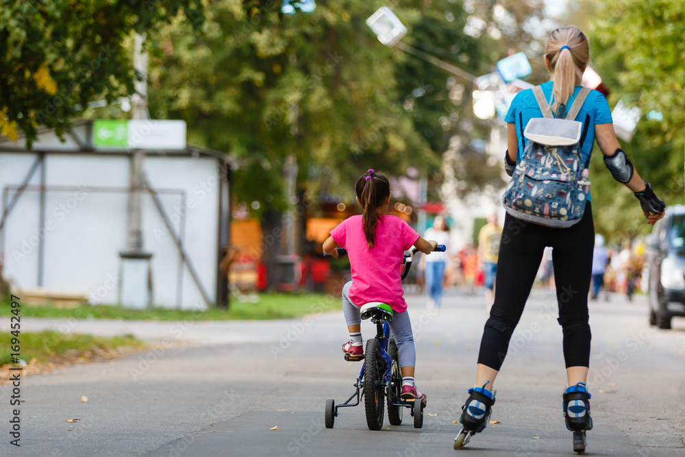 A young mother roller skating. her Daughter riding a bicycle A young mother roller skating. her Daughter riding a bicycle