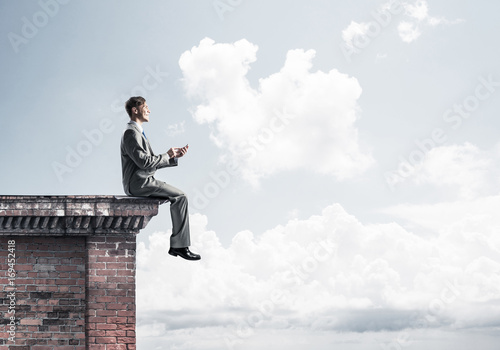 Man on roof edge reading book and cityscape at background