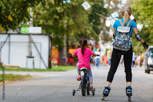 A young mother roller skating. her Daughter riding a bicycle © Angelov