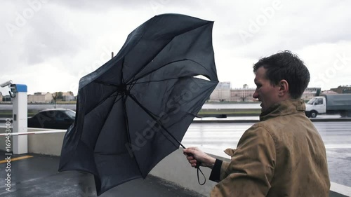 Man in jacket with umbrella standing outdoors. The gust of wind pulls umbrella out of hand