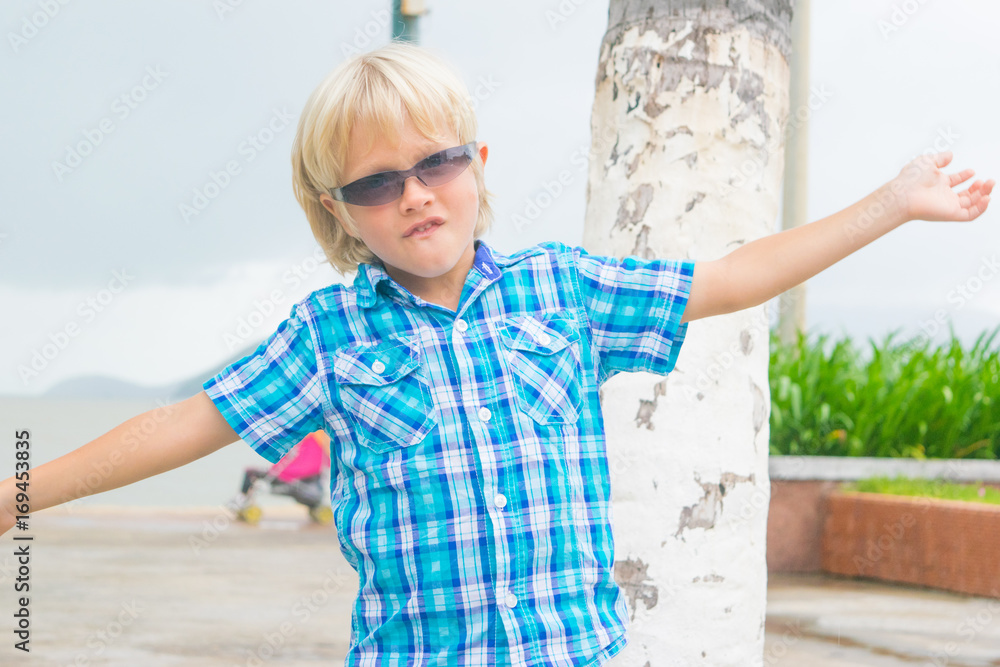 A cool blond boy in sunglasses walking in a park