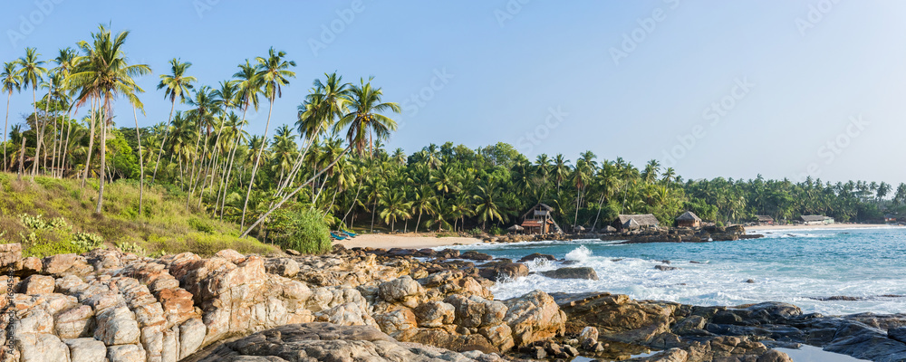 Panoramic view of the beach with the old tropical bungalow and traditional wooden fishing boats in Sri Lanka.