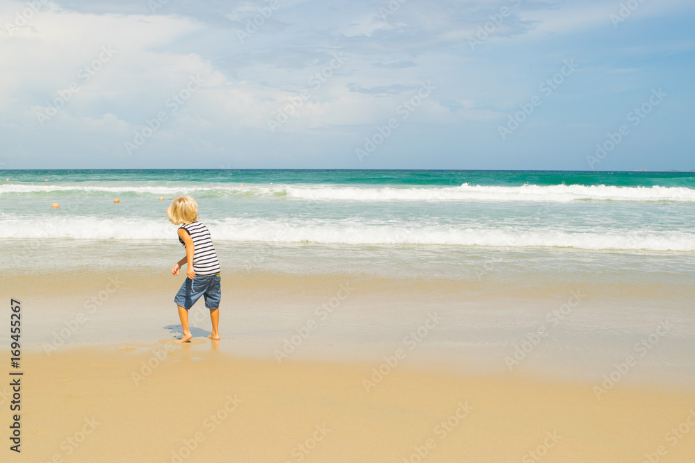 A blond boy (child) throwing a coin in water at a sea shore (beach), Nha Trang, Vietnam