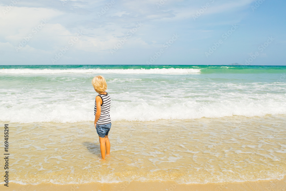 A thoughtful blond boy (child) staying in water at a sea shore (beach), Nha Trang, Vietnam
