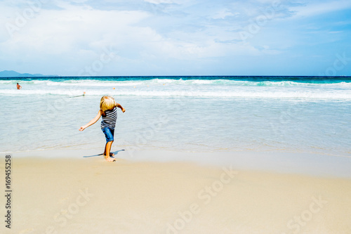 A blond boy (child) throwing a coin in water at a sea shore (beach), Nha Trang, Vietnam