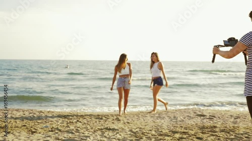 Filmaker woman shooting with camera and two dancing female models on beach at sunset slow motion photo