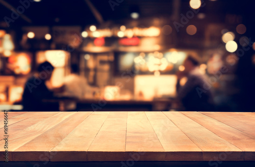 Wood table top with blur light bokeh in night cafe background .Lifestyle and celebration concept