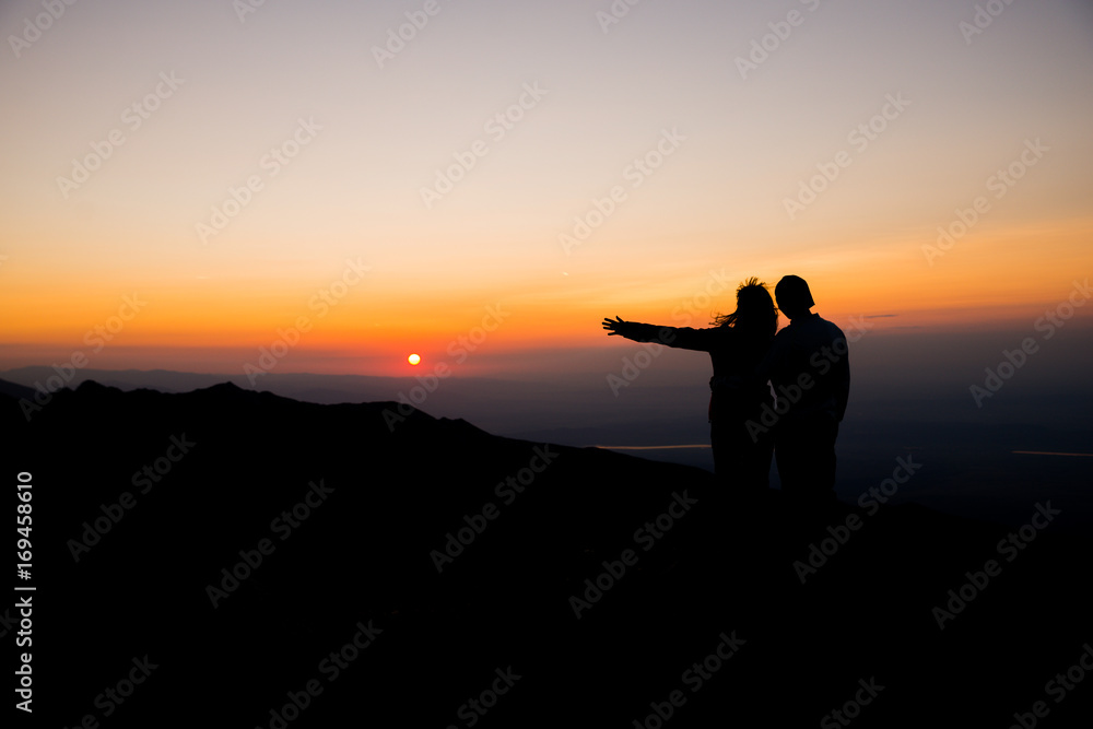 Couple watching sunset over the mountains. Holding each other. Romantic scenery. Friendship.