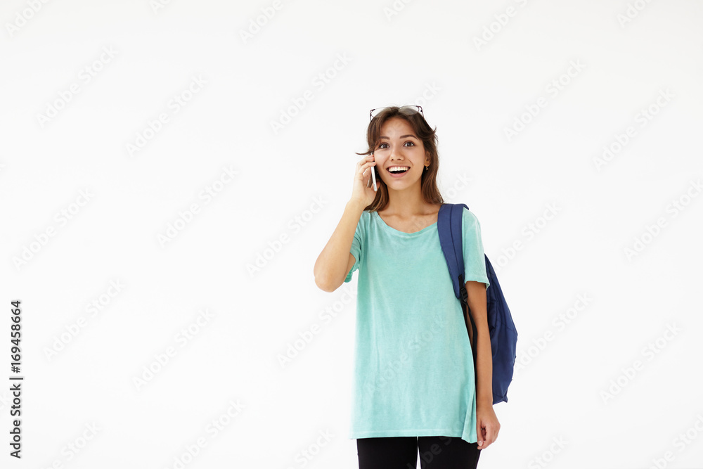 Happy Latin student girl carrying backpack and talking on mobile phone with friend, making appointment for walk after lectures at college, having excited cheerful look, posing isolated in white studio Happy Latin student girl carrying backpack and talking on mobile phone with friend, making appointment for walk after lectures at college, having excited cheerful look, posing isolated in white studio