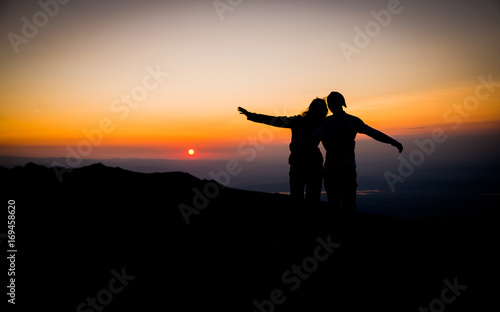 Couple watching sunset over the mountains. Holding each other. Romantic scenery. Friendship. © icephotography