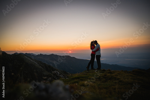 Couple watching sunset over the mountains. Holding each other. Romantic scenery. Friendship.