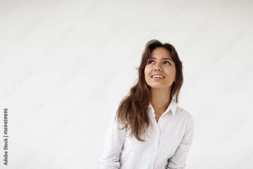 Isolated studio shot of beautiful woman employee wearing white formal shirt looking up and smiling cheerfully, daydreaming, planning holidays during break at office with blank copy space wall Isolated studio shot of beautiful woman employee wearing white formal shirt looking up and smiling cheerfully, daydreaming, planning holidays during break at office with blank copy space wall