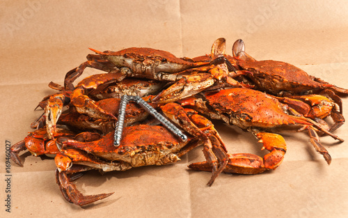 Pile of steamed and seasoned Chesapeake Bay blue claw crabs / on a wood cutting board with a steel cracker and a wood bowl of spicy,seasoning on brown paper table covering
