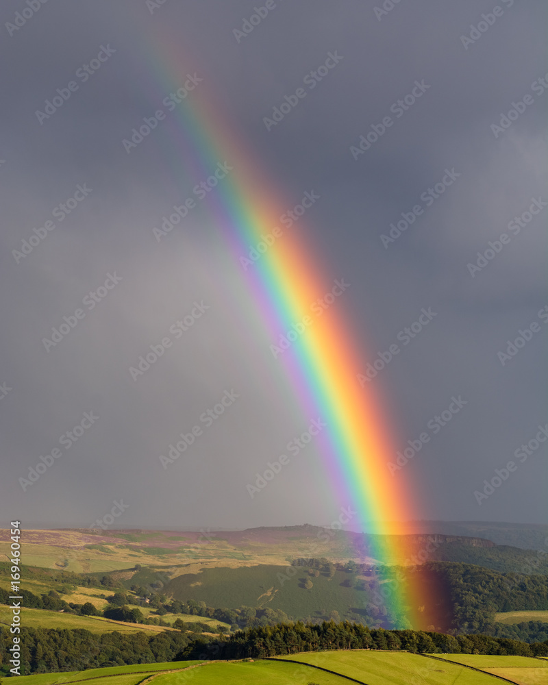 Colourful rainbow shining down on valley with dark moody clouds in background.